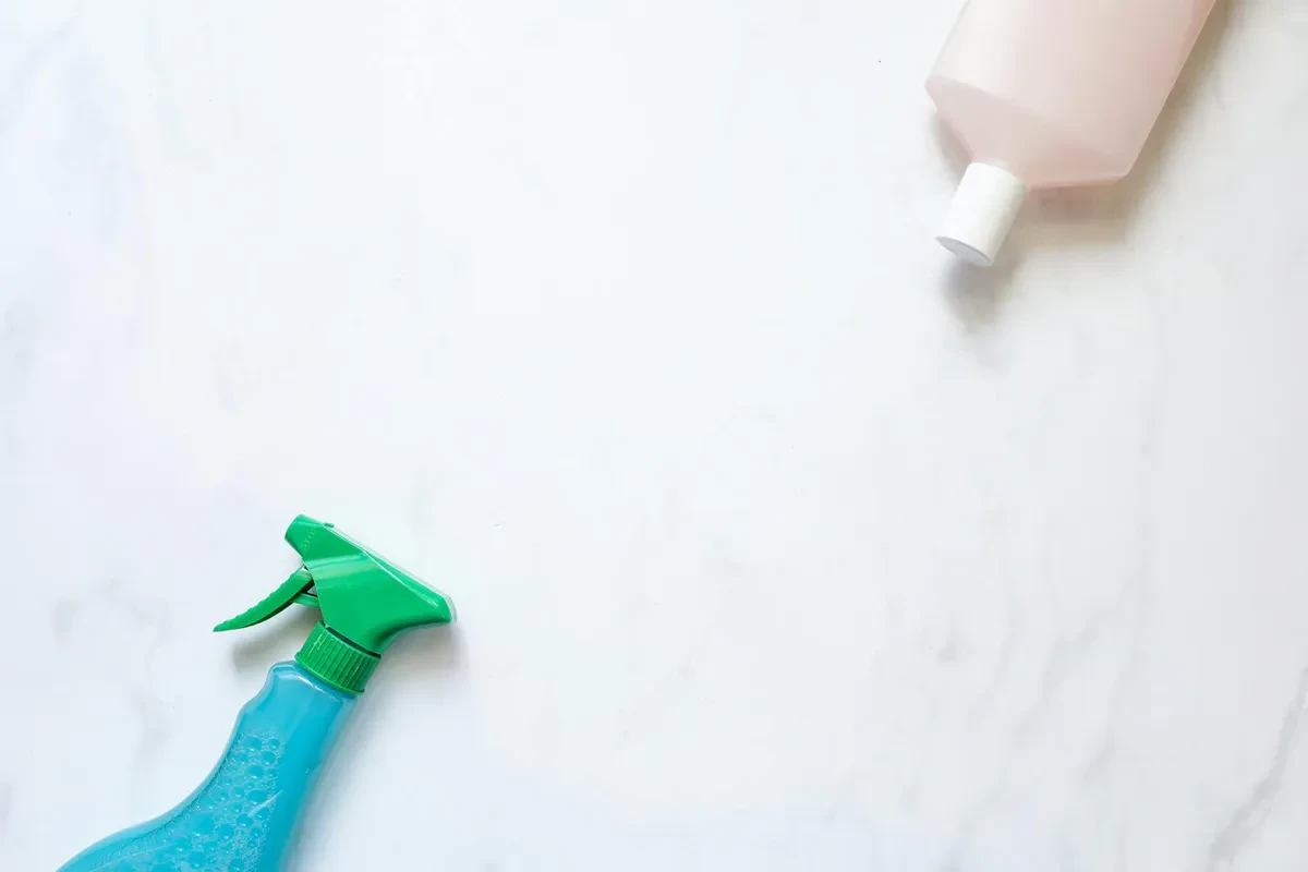 A blue spray bottle and a pink refill bottle on white marble