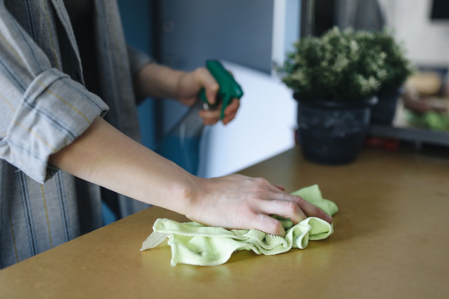 A hand wiping a kitchen counter with a cloth next to a spray bottle